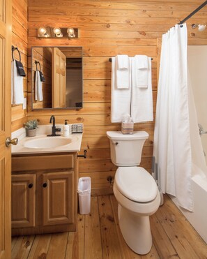 A wooden-paneled bathroom with a sink, mirror, and toilet. - Red Feather Cabins 282 (Boone)