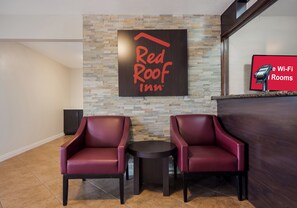A Red Roof Inn reception area with two leather chairs, a small table, and a stone wall. - Red Roof Inn Madisonville (Madisonville)