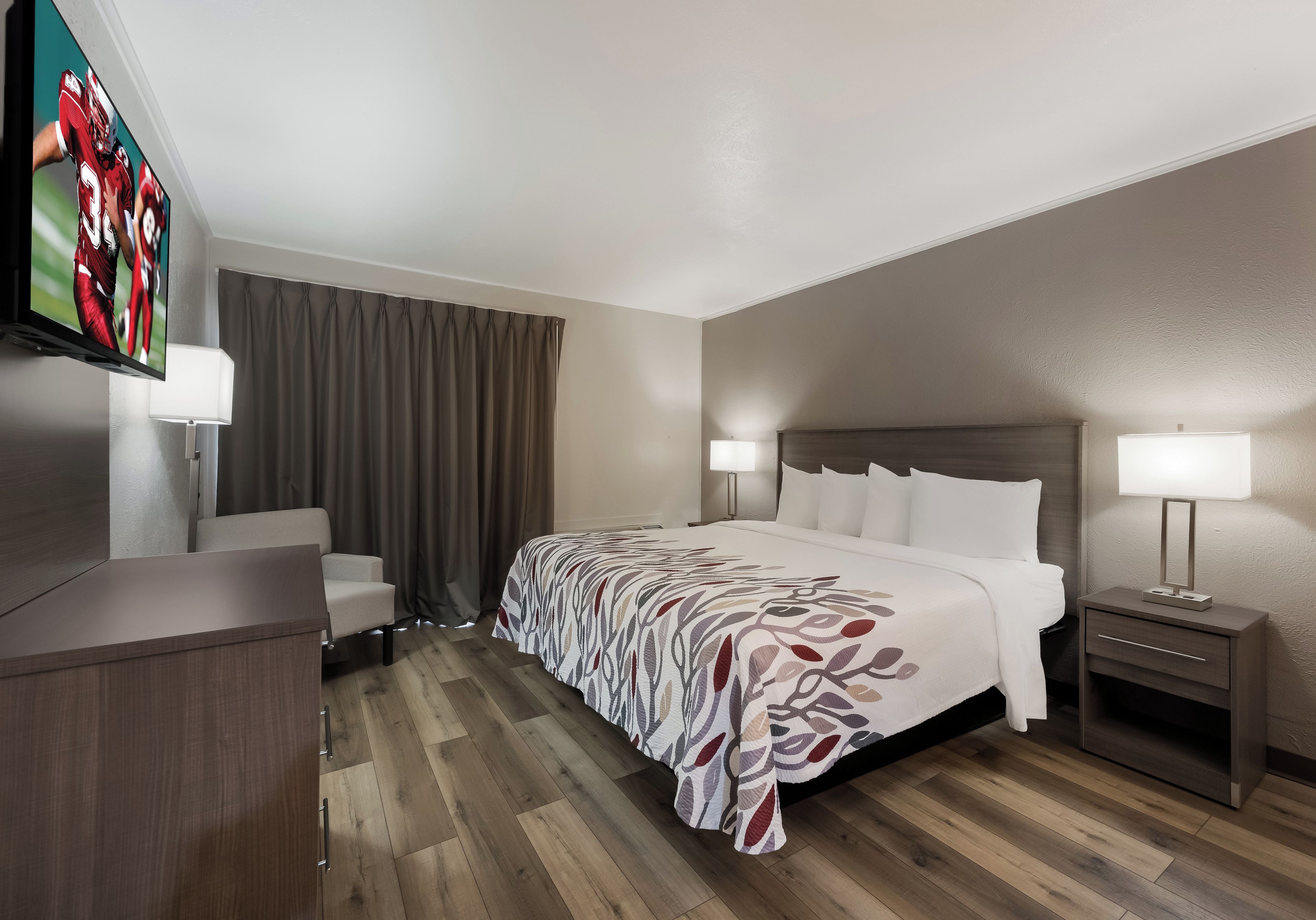 A hotel room with a bed, bedside tables, a desk, a chair, and a television.