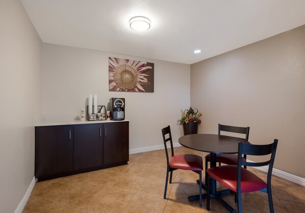 A dining area with a dark wooden cabinet, two chairs with red cushions, a round table, and a wall-mounted flower arrangement. - Red Roof Inn Madisonville (Madisonville)