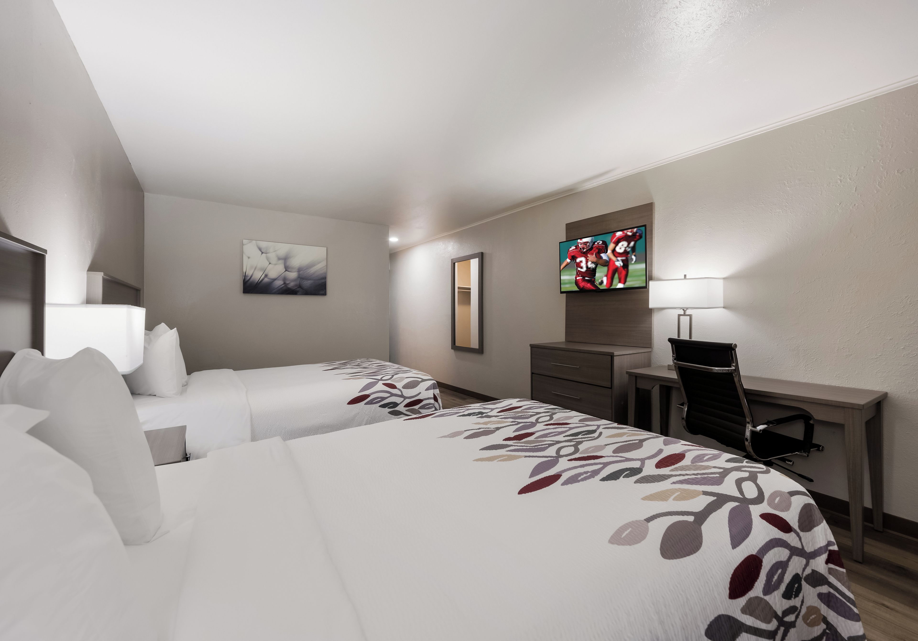 Una habitación de hotel con dos camas, un escritorio, una silla, un televisor y una l ámpara.