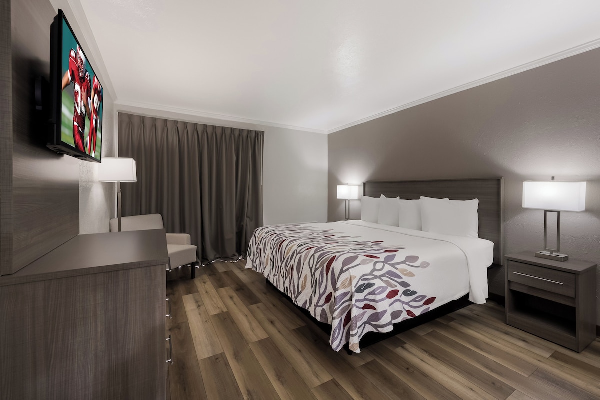 A hotel room with a bed, bedside tables, a TV mounted on the wall, and a wooden floor.