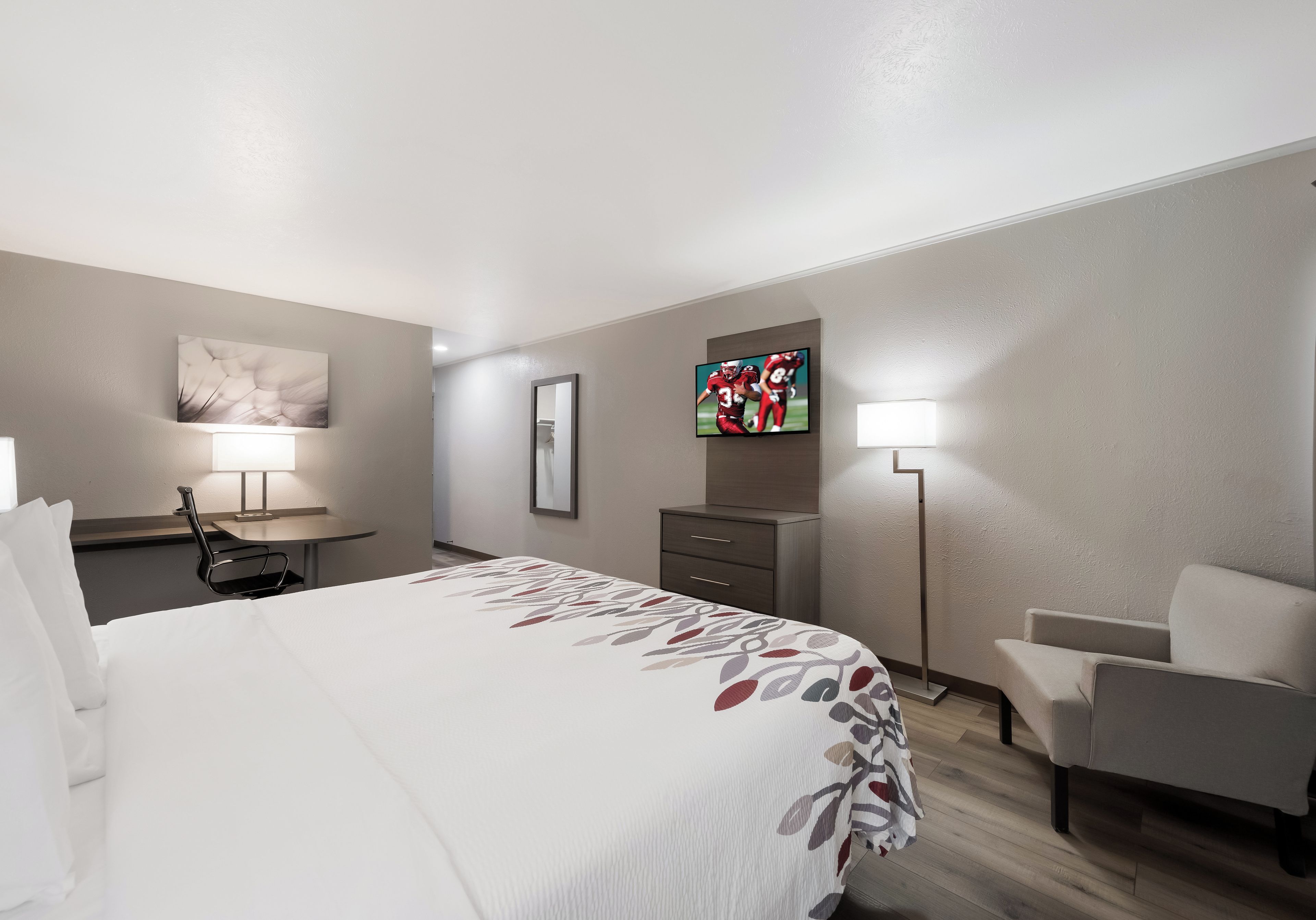 A hotel room with a bed, a desk, a chair, a television, and a lamp.