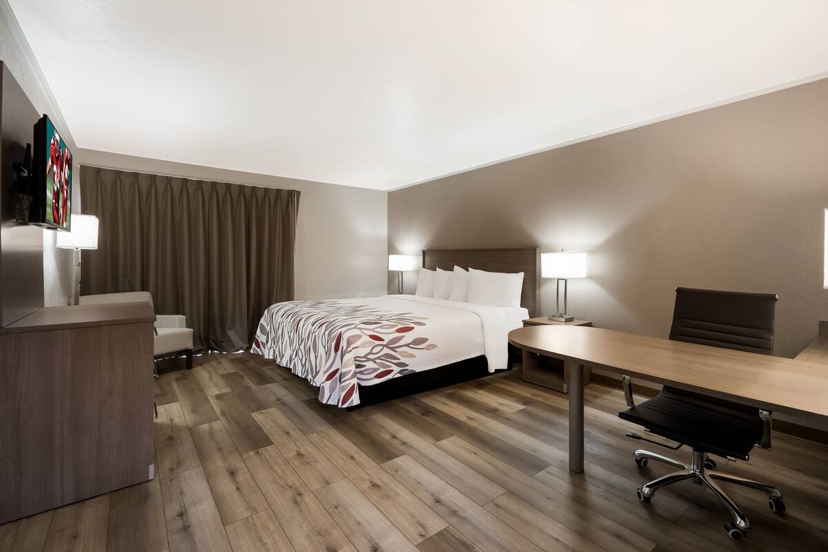 A hotel room with a bed, desk, chair, and a TV mounted on the wall.