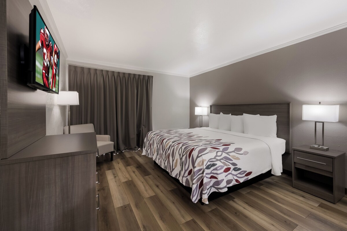A hotel room with a bed, bedside tables, a TV, and a desk.
