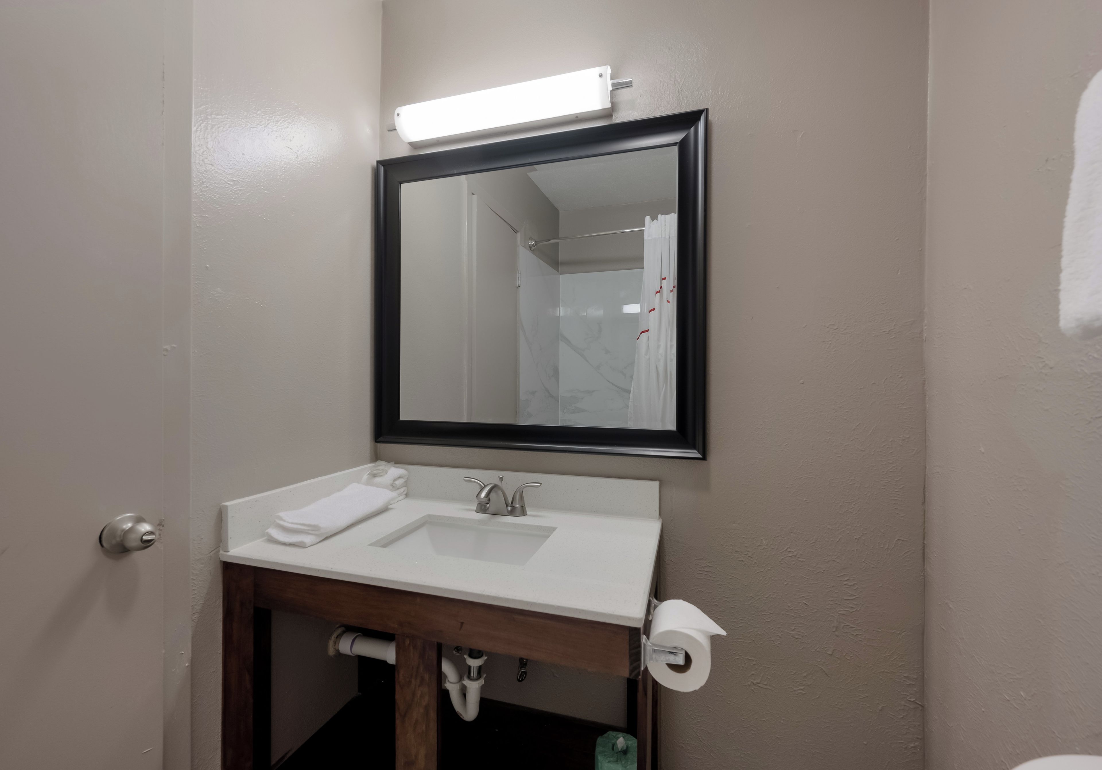 Un baño con un lavamanos blanco, un espejo y un dispensador de papel higiénico.