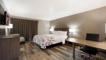 Una habitación de hotel con cama, escritorio, silla y televisor sobre un pedestal.