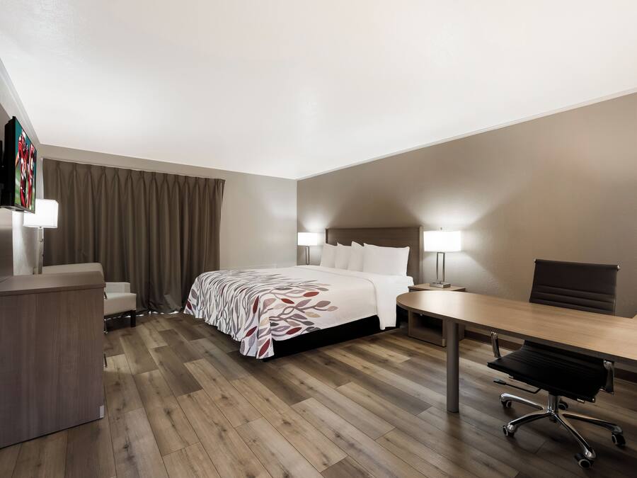 Een hotelkamer met een bed, bureau, stoel en een televisie op een standaard.