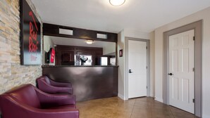 A hotel lobby with a reception desk, a mirror, a wall-mounted sign, and a row of purple chairs. - Red Roof Inn Madisonville (Madisonville)