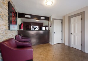 Um hall de hotel com balcão de recepção, espelho, placa na parede e fileira de cadeiras roxas.
