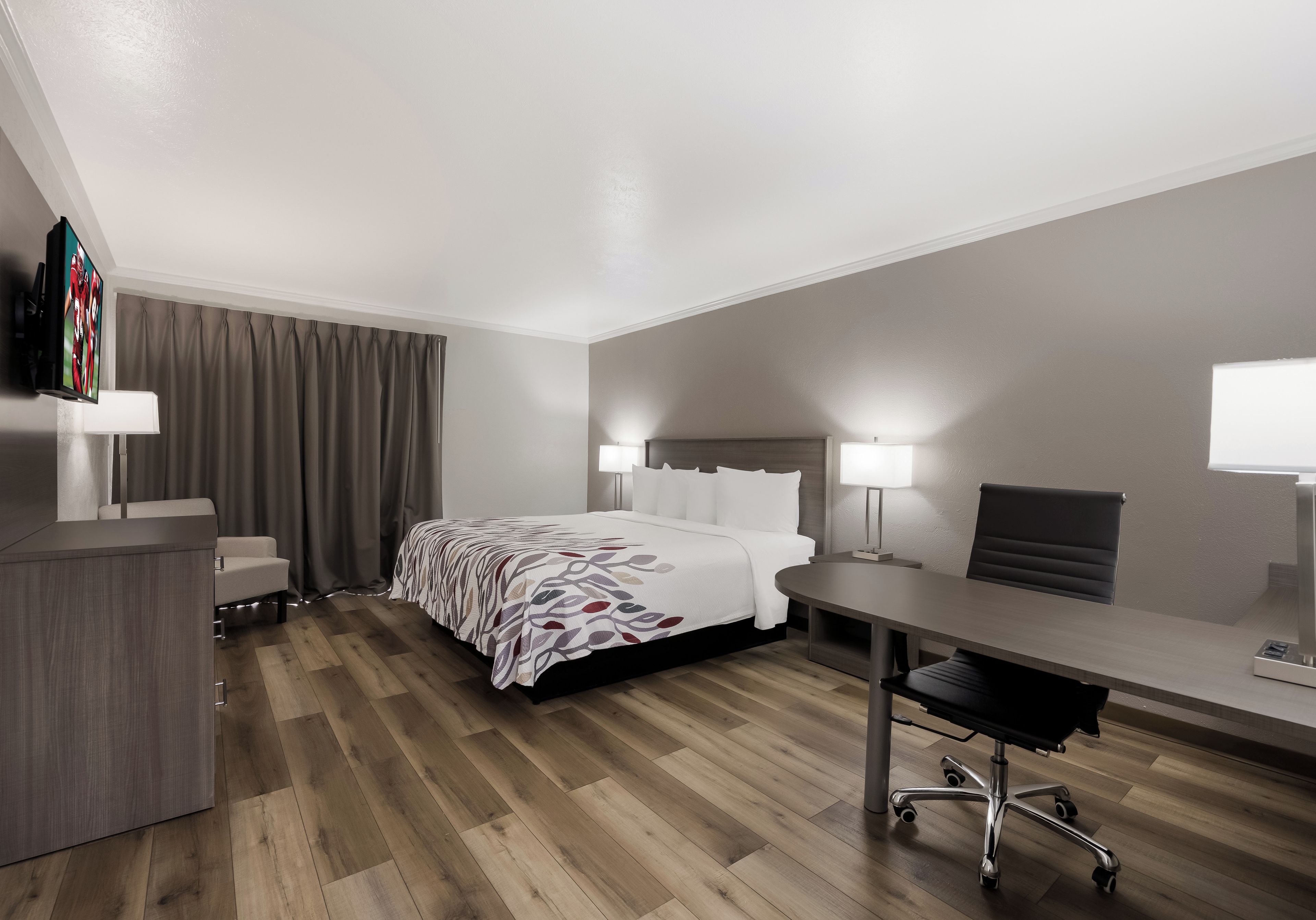 Una habitación de hotel con cama, escritorio, silla y televisor sobre un soporte.