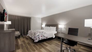 Una habitación de hotel con cama, escritorio, silla y televisor sobre un soporte.