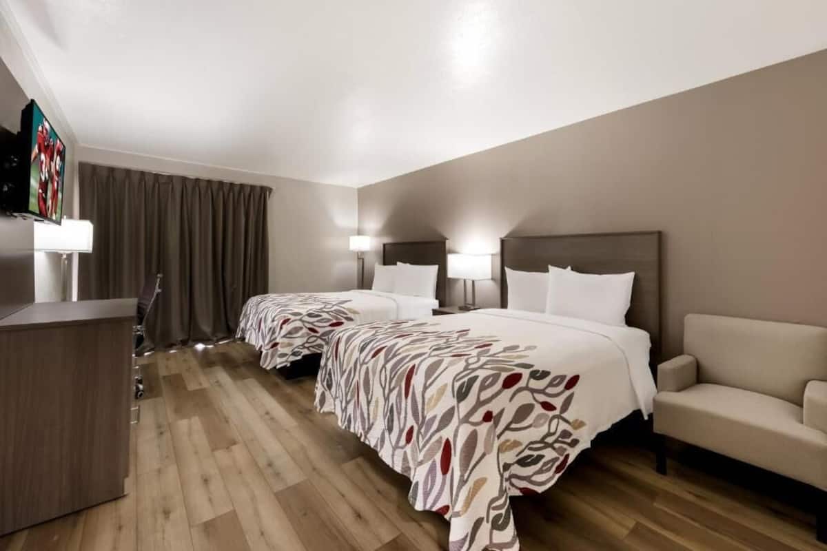 A hotel room with two beds, a desk, a sofa, and a TV.