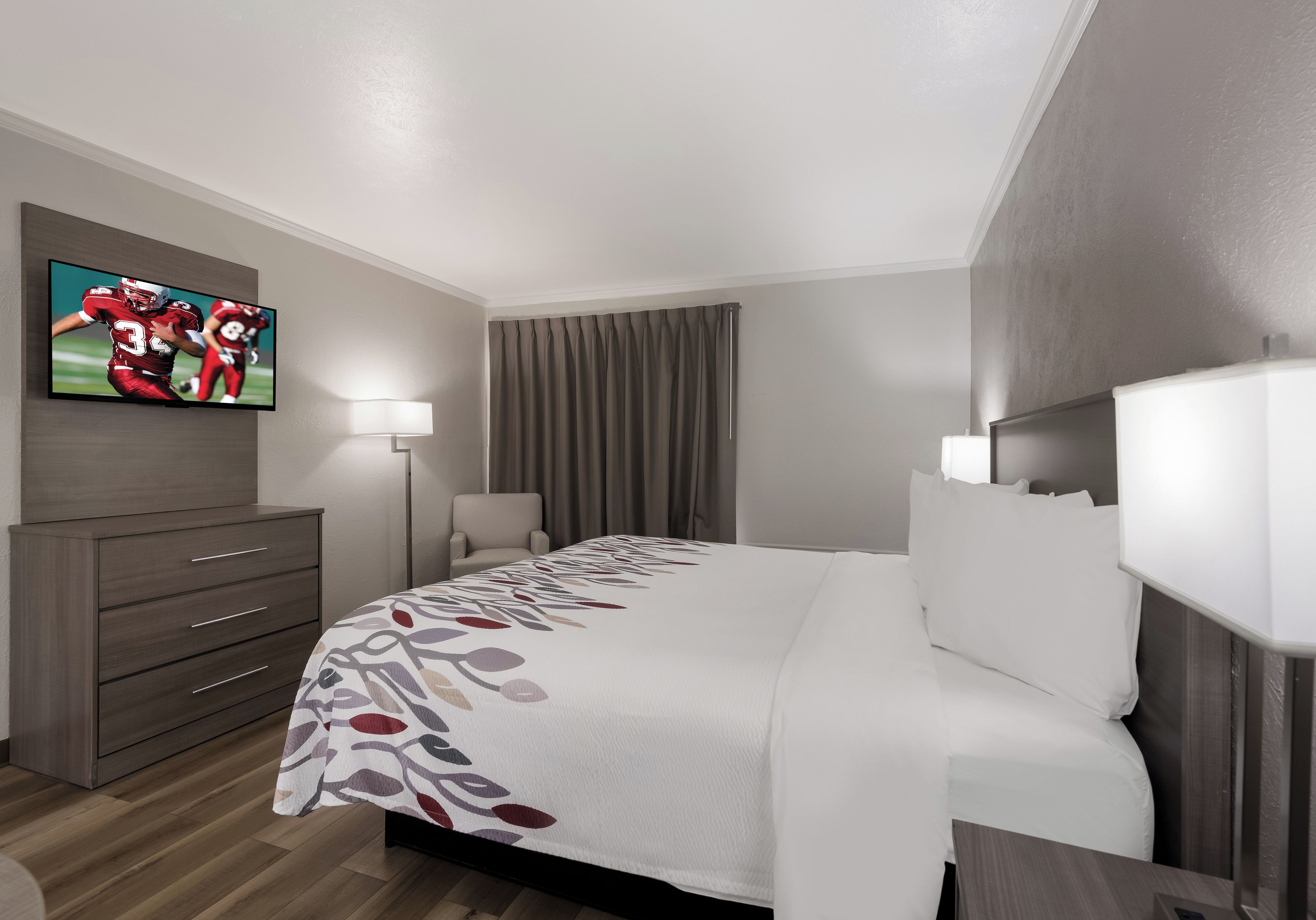 A hotel room with a bed, a TV mounted on the wall, a desk, and a chair.