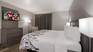 A hotel room with a bed, a TV mounted on the wall, a desk, and a chair. - Red Roof Inn Madisonville (Madisonville)