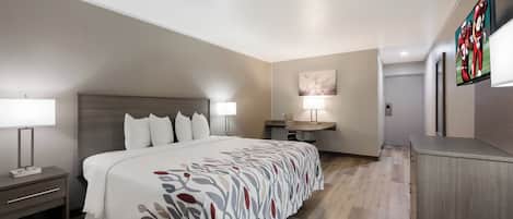 A hotel room with a bed, bedside tables, a desk, a chair, a lamp, and a TV mounted on the wall.