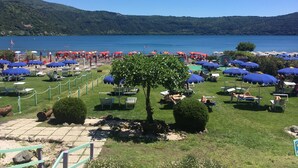 Ein Seehotel mit Liegestühlen und Sonnenschirmen, umgeben von üppigem Grün und klarem Seeblick.