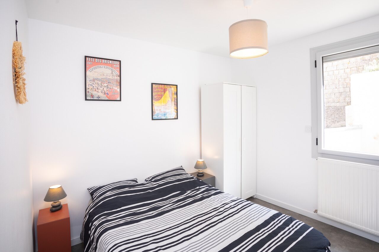 A bedroom with a bed, two bedside lamps, a hanging lamp, a wardrobe, and two framed posters on the wall.