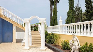 A white balustrade, a statue, and a staircase leading to a building with a blue tiled wall.