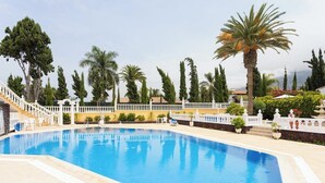 A swimming pool with a white fence, palm trees, and a staircase leading to a building.