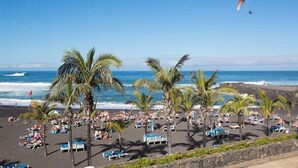 A beach with palm trees, lounge chairs, and a parasail in the background.