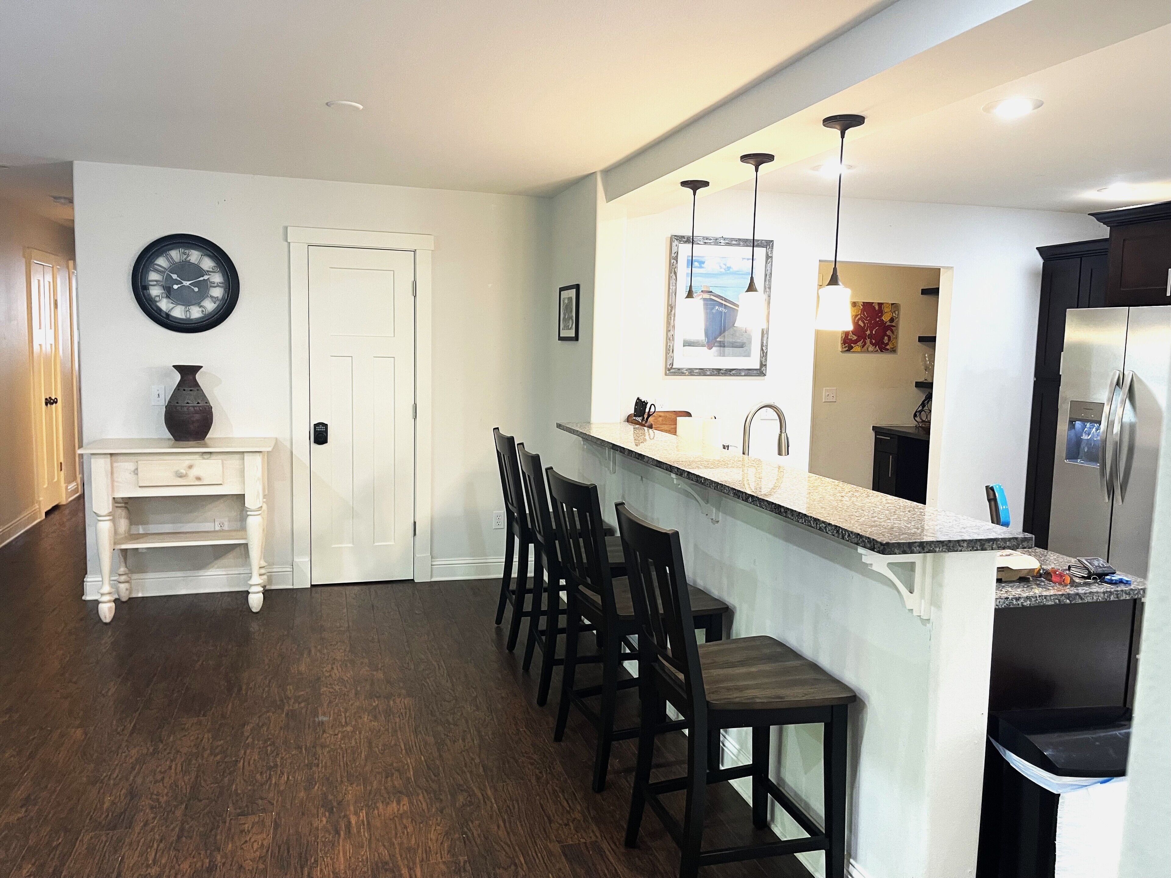 A kitchen with a white door, a clock, a vase, and a refrigerator.