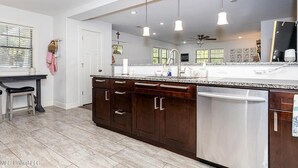 A modern kitchen with dark wooden cabinets, a stainless steel dishwasher, and pendant lighting. - Beach Cottage Lafayette Circle (Ocean Springs)