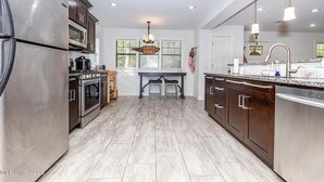 A modern kitchen with stainless steel appliances, a central island, and a window overlooking the backyard. - Beach Cottage Lafayette Circle (Ocean Springs)
