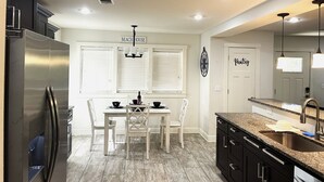 A modern kitchen with a stainless steel refrigerator, white cabinetry, a dining table with chairs, and a kitchen island with a sink. - Beach Cottage Lafayette Circle (Ocean Springs)