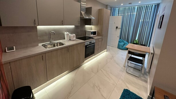 A modern kitchen with a built-in oven, microwave, and sink. There is a small dining area with a table and chairs. - Themed Stunning 1-bed Apartment in London (London)
