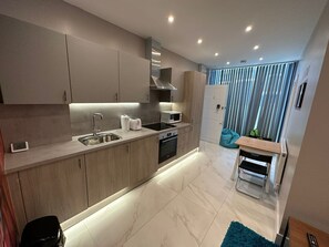 A modern kitchen with a built-in oven, microwave, and sink. There is a small dining area with a table and chairs. - Themed Stunning 1-bed Apartment in London (London)