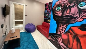 A modern room with a TV, a bean bag, a red couch, and a large mural on the wall. - Themed Stunning 1-bed Apartment in London (London)