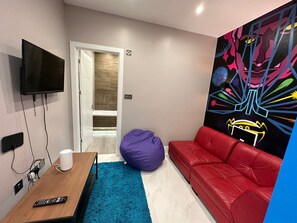 A modern room with a TV, a wooden table, a red couch, a purple bean bag, and a colorful mural. - Themed Stunning 1-bed Apartment in London (London)