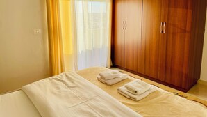 A bedroom with a bed, a wooden wardrobe, and a window with sheer curtains. - EasyTrip Family - 2 bedrooms - City Center_417 (Divjakë)