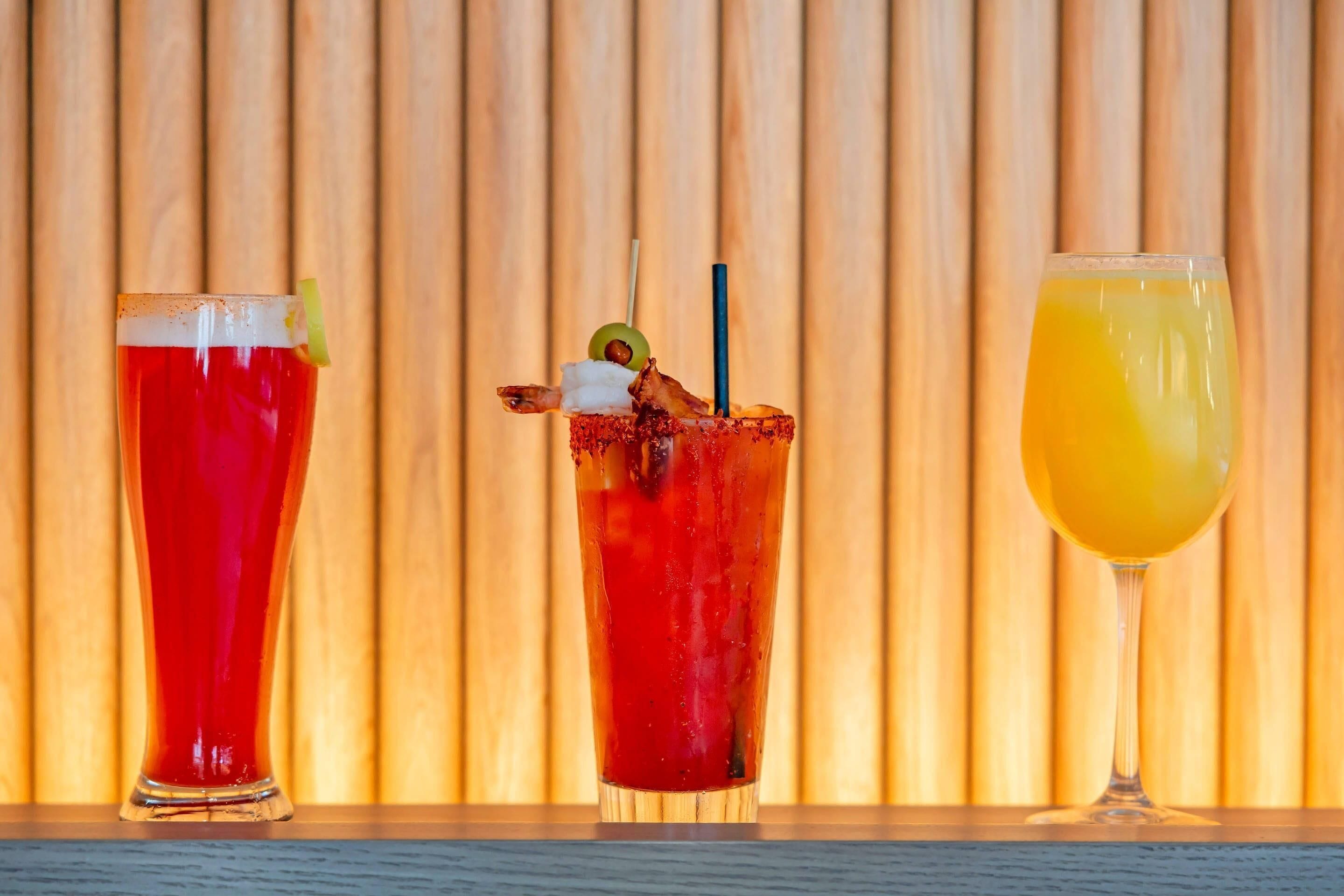 Three glasses of beverages on a wooden surface against a wooden background.