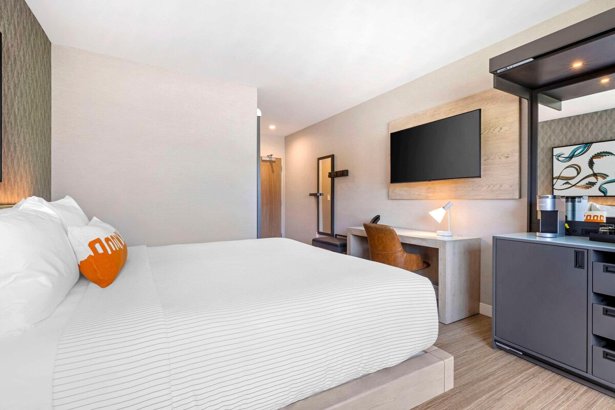 Una habitación de hotel moderna con una cama grande, un escritorio, un televisor de pantalla plana y una cafetera.