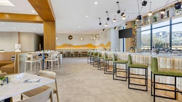 A modern restaurant with a long counter, green cushioned chairs, and a view of mountains through large windows.