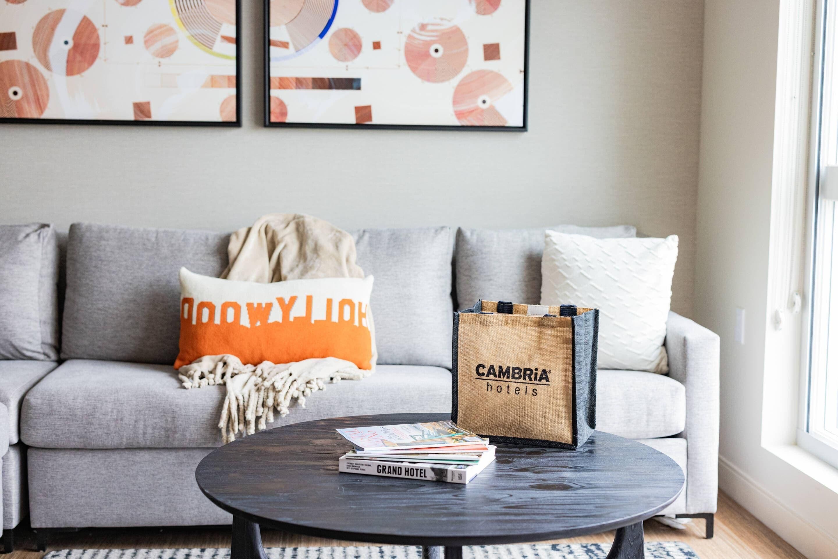 Una sala de estar moderna con un sofá gris, una mesita de centro con libros y una bolsa de 'Cambria hotels'.