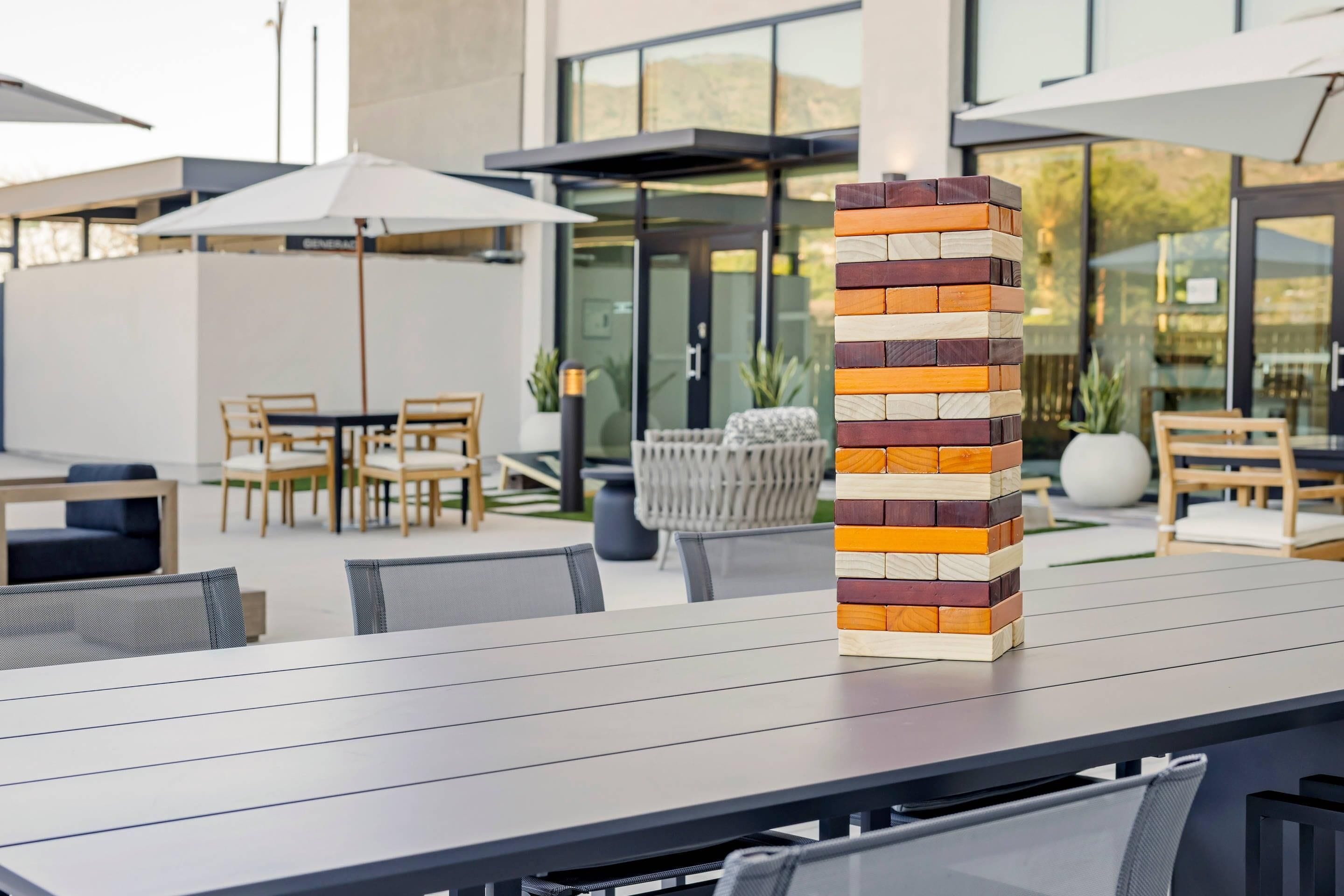 An outdoor dining area with a modern design, featuring a stack of wooden blocks on a table and a seating arrangement with chairs and umbrellas.
