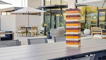 An outdoor dining area with a modern design, featuring a stack of wooden blocks on a table and a seating arrangement with chairs and umbrellas.