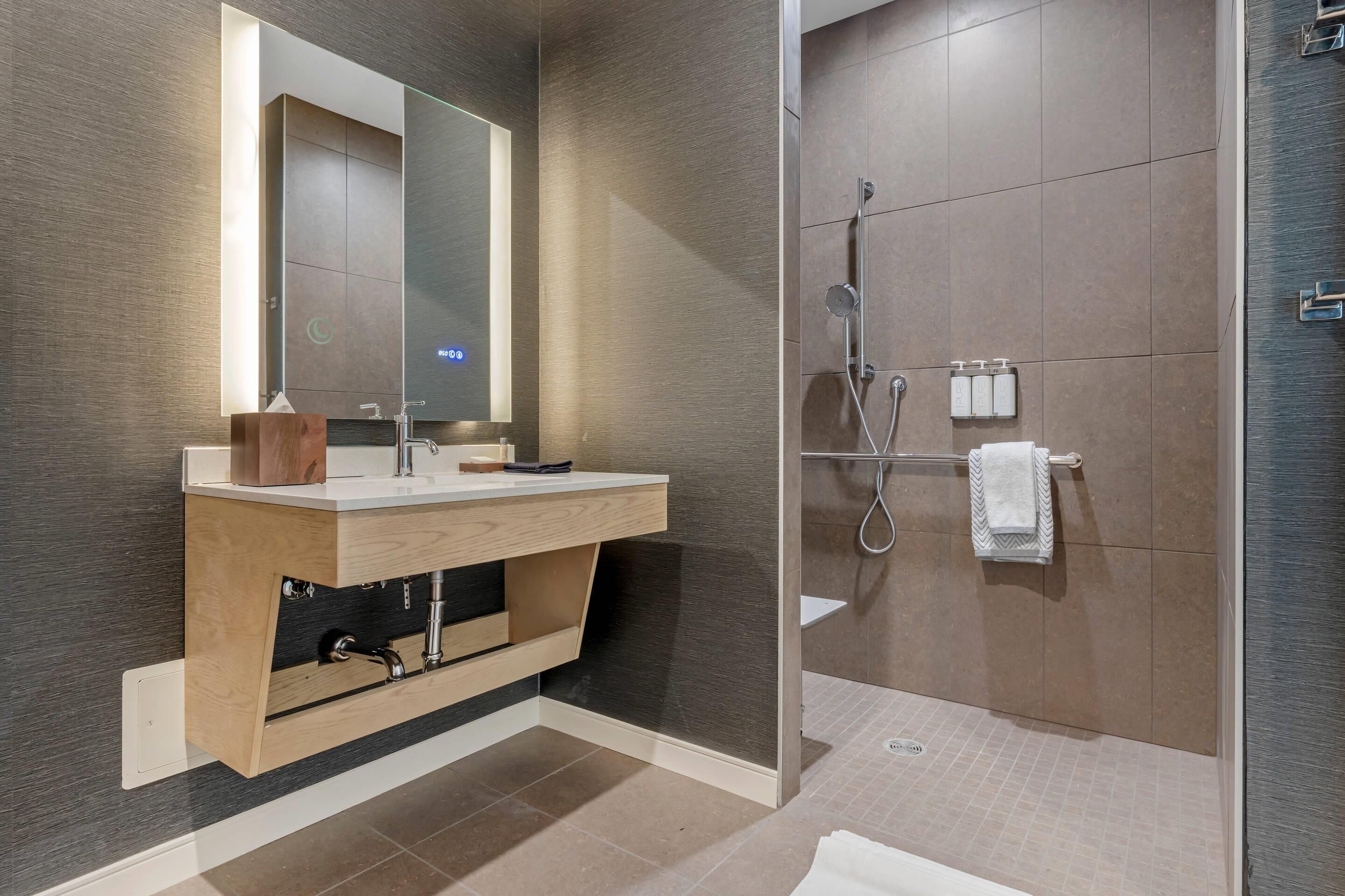 A modern bathroom with a wooden vanity, a large mirror, a shower area, and a towel rack.