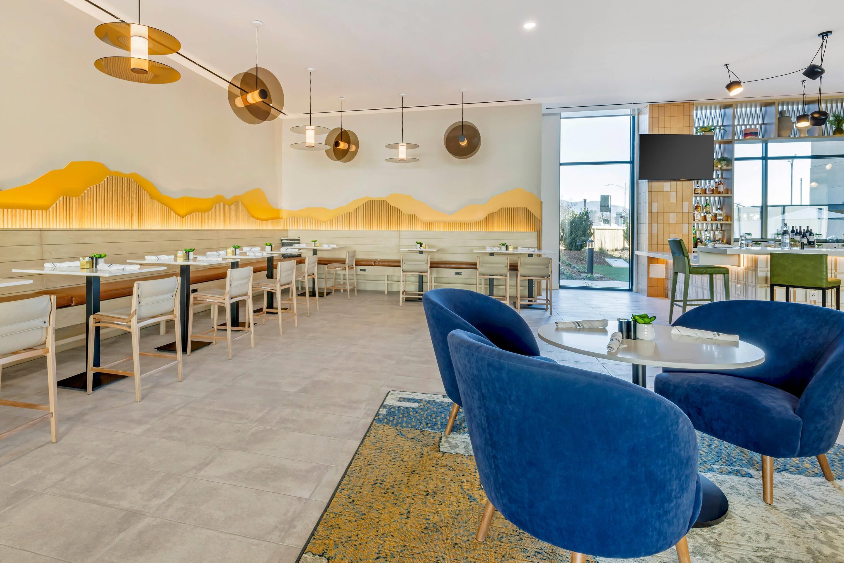 Un restaurante moderno con una barra larga, sillas azules e iluminación colgante.
