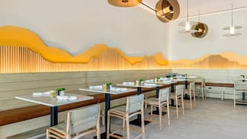 Un interior de restaurante moderno con mesas comunitarias largas, bancos acolchados e iluminación contemporánea.