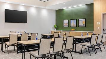 A conference room with multiple tables and chairs, a large flat-screen TV, framed pictures on the wall, and a green accent wall.
