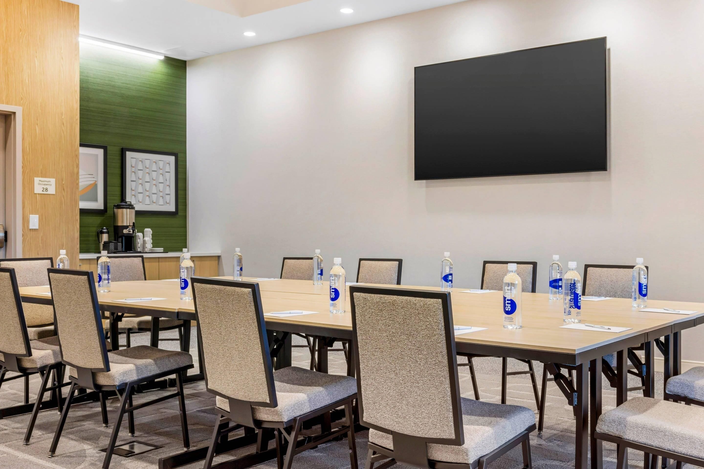 A conference room with a large table, chairs, a projector screen, and water bottles.