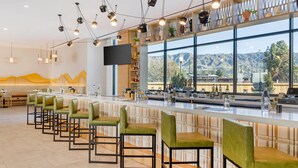 A modern bar area with green bar stools, a long counter, and a large window offering a mountain view. - Cambria Hotel Burbank Airport (Burbank)