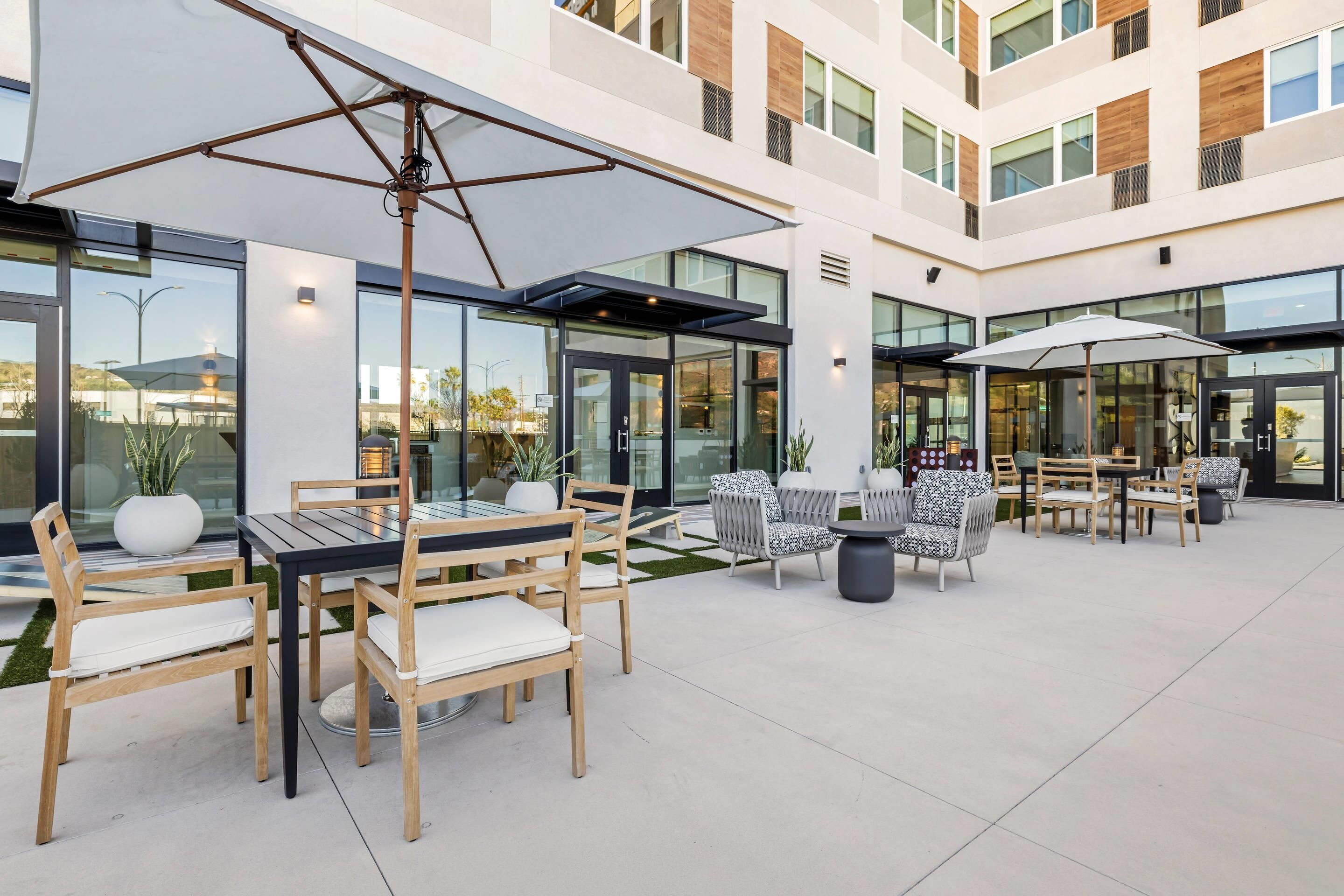 An outdoor patio area with tables and chairs, large umbrellas, and potted plants.