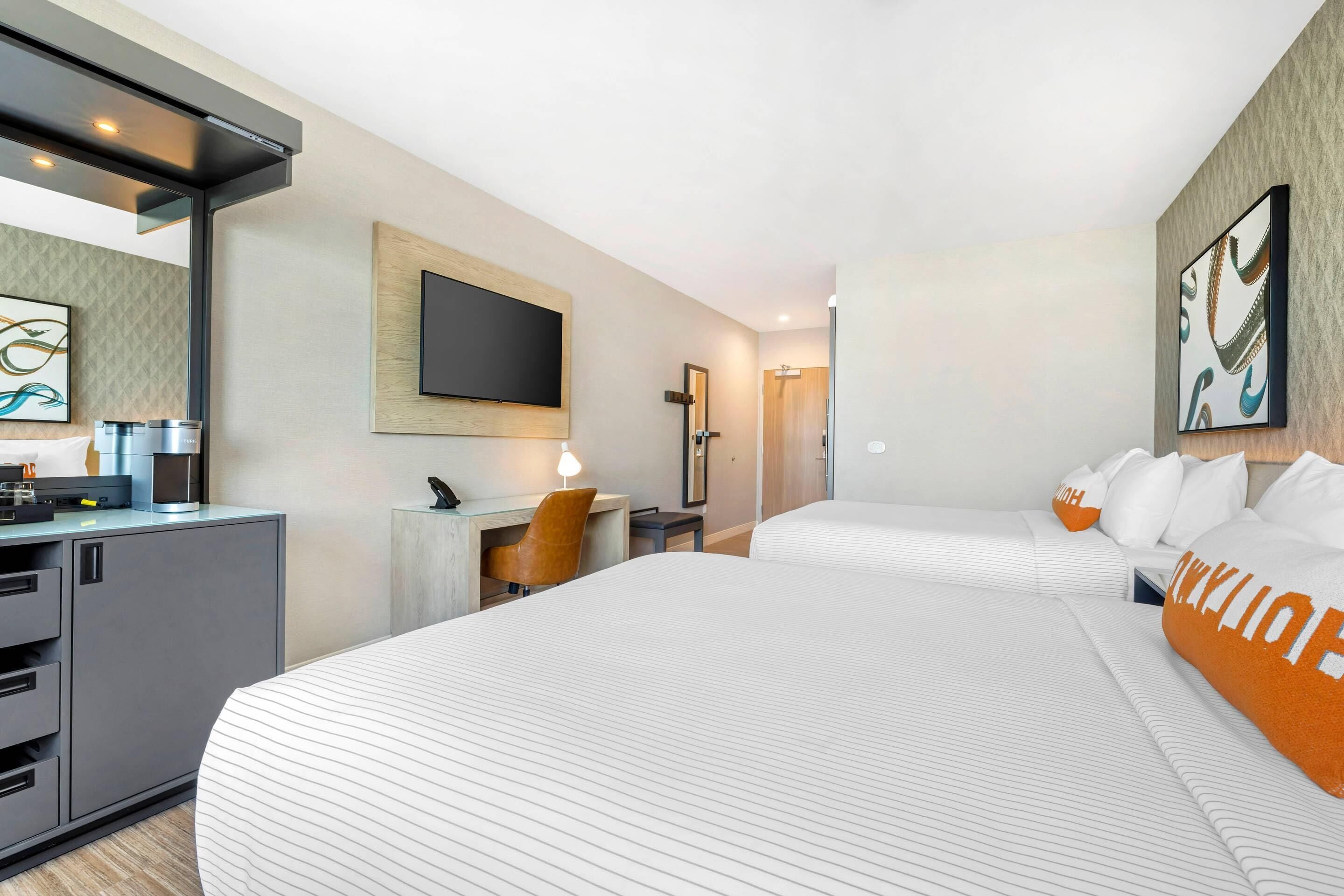 A hotel room with two beds, a desk, a chair, a television, and a minibar.