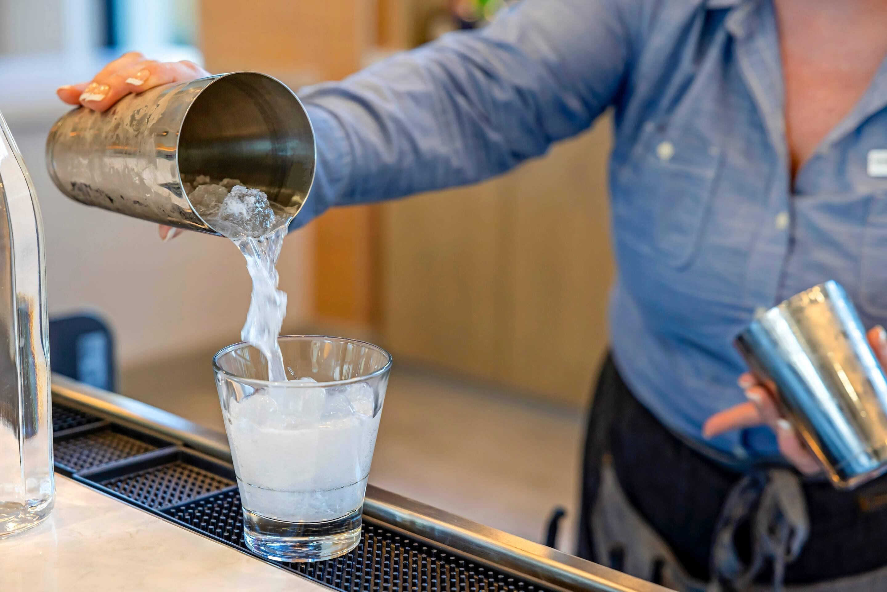 Una persona vertiendo un líquido desde un recipiente metálico en un vaso.