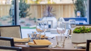 A dining table set with wine glasses, plates, and cutlery, with a view of a wooden fence and greenery outside. - Cambria Hotel Burbank Airport (Burbank)